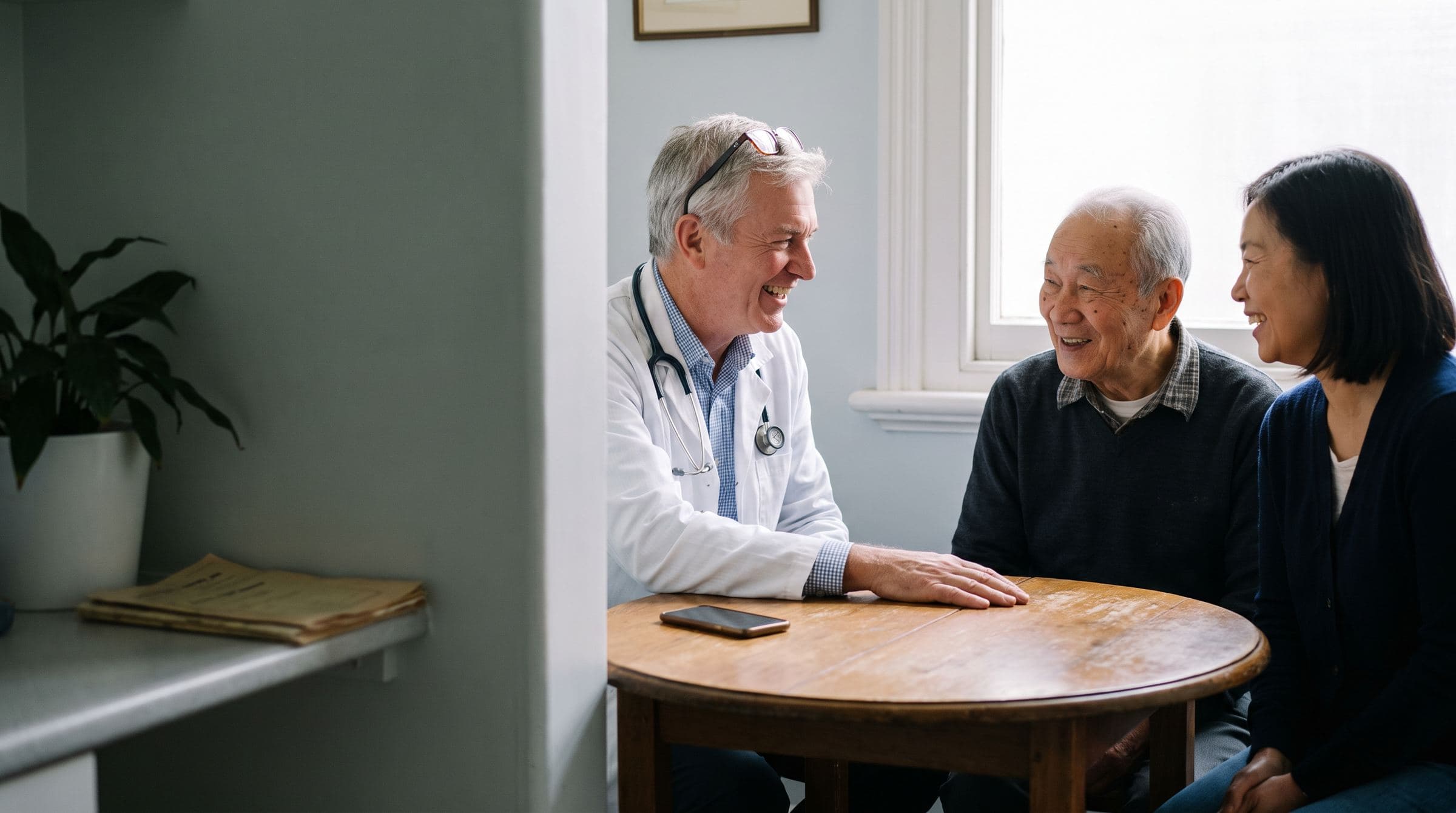 Doctor laughing with an older patient and his daughter during an exam room visit