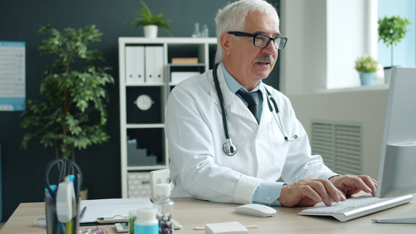 A physician dictating a note at his Mac workstation in a bright clinic office